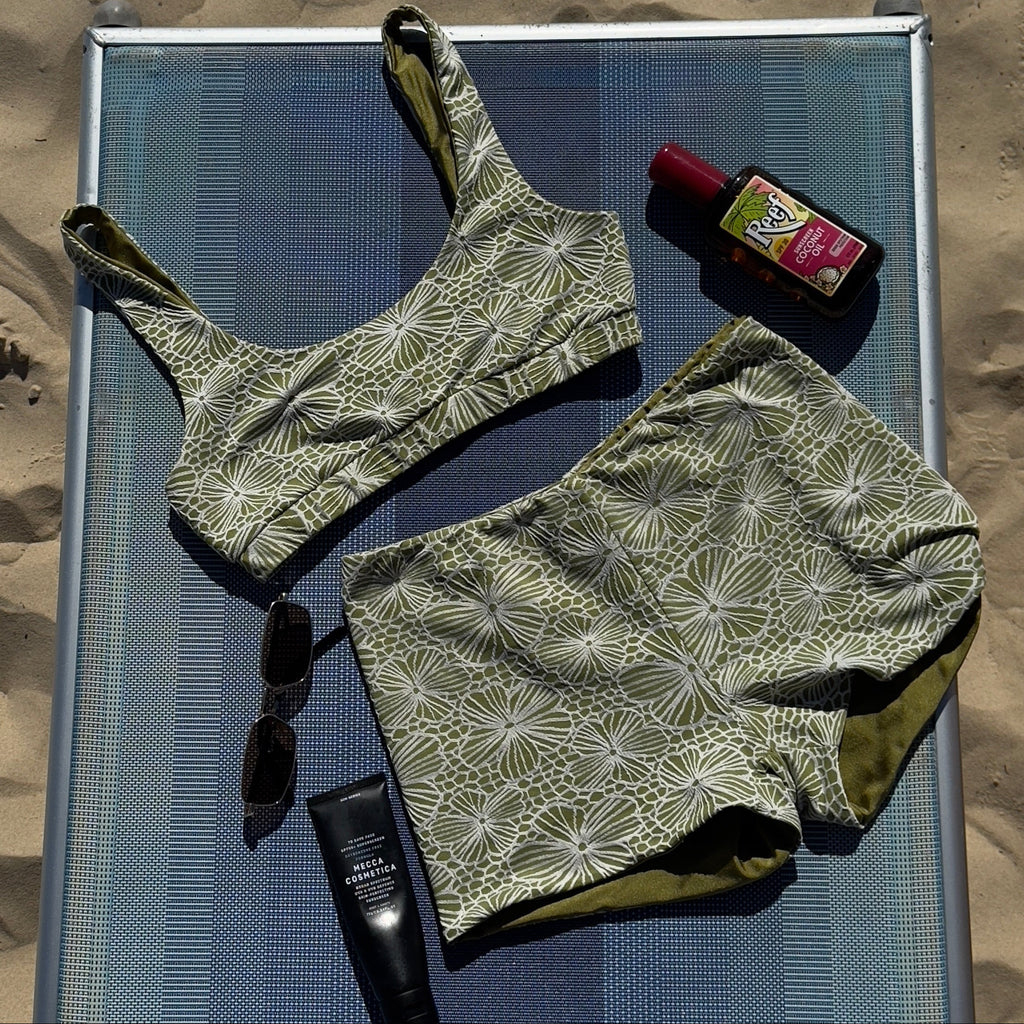 Green patterned swimsuit on a sunbed with sunscreen and lip balm on a sandy background
